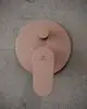 Wandmontierte Armatur in Rosé von Ideal Standard mit einem großen Drehknopf und farbigen Indikatoren für heißes und kaltes Wasser auf einer grauen Oberfläche.